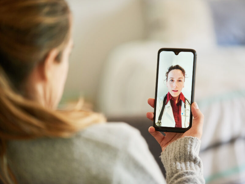 Woman using a smart phone app to consult with a doctor in real time while sitting on her living room sofa at home.